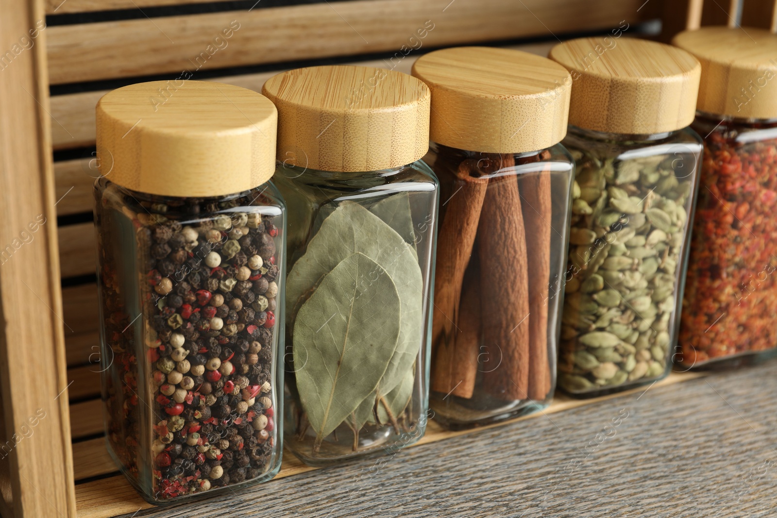 Photo of Different spices in glass jars on grey wooden table, closeup