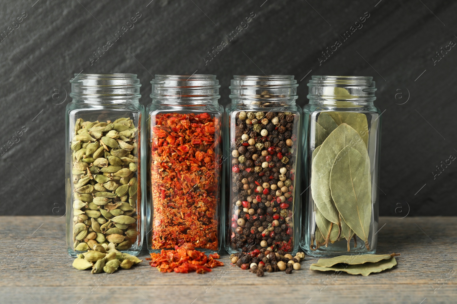 Photo of Different spices in glass jars on grey wooden table, closeup