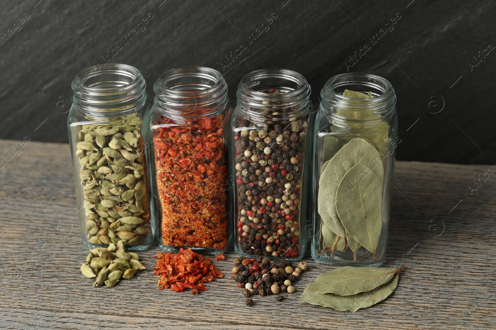 Photo of Different spices in glass jars on grey wooden table, closeup