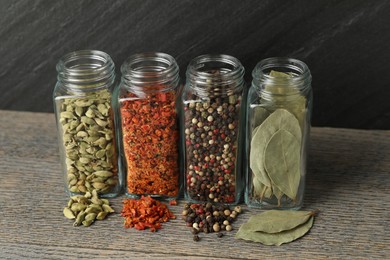 Different spices in glass jars on grey wooden table, closeup