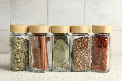 Different spices in glass jars on light textured table, closeup