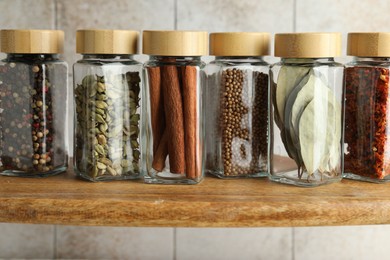 Photo of Different spices in glass jars on wooden shelf, closeup