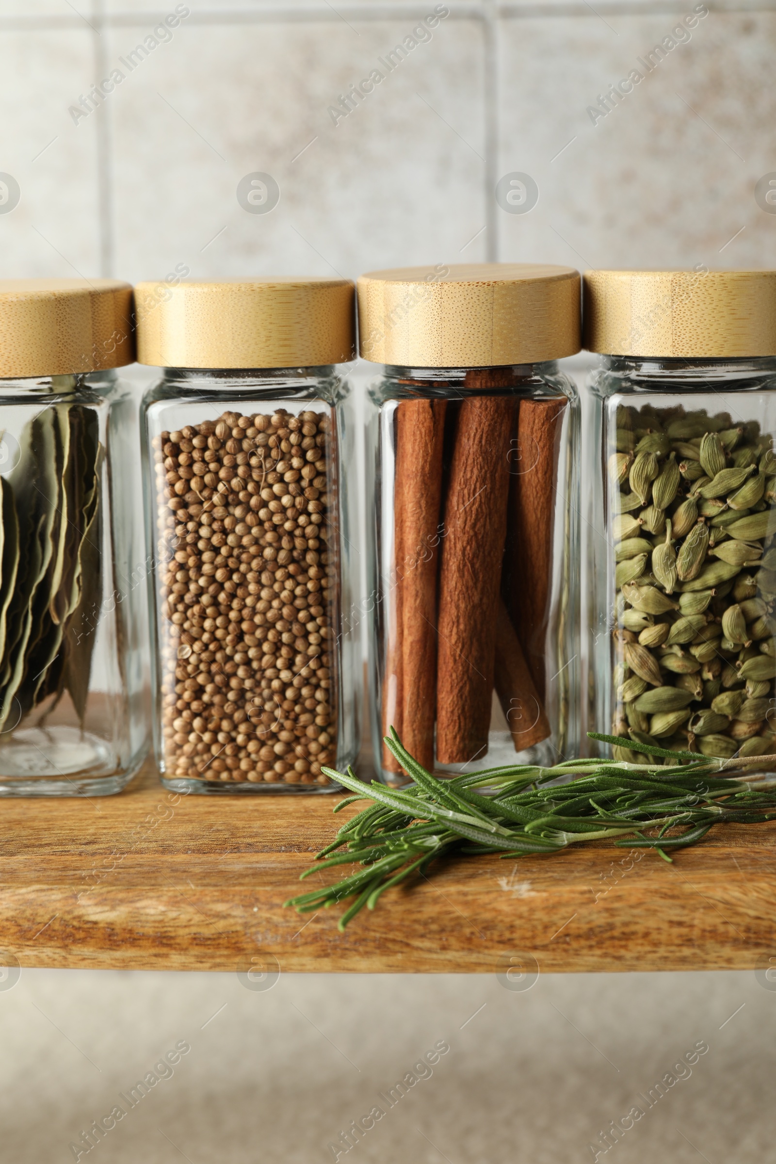 Photo of Different spices in glass jars on wooden board, closeup