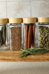 Different spices in glass jars on wooden board, closeup