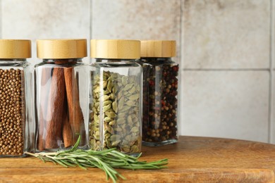 Photo of Different spices in glass jars on wooden board, closeup. Space for text