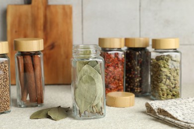 Photo of Different spices in glass jars on light textured table, closeup