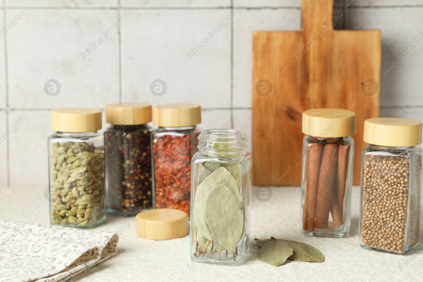 Photo of Different spices in glass jars on light textured table, closeup