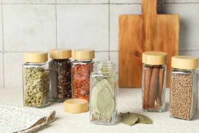 Photo of Different spices in glass jars on light textured table, closeup