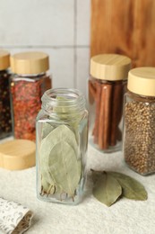 Photo of Different spices in glass jars on light textured table, closeup