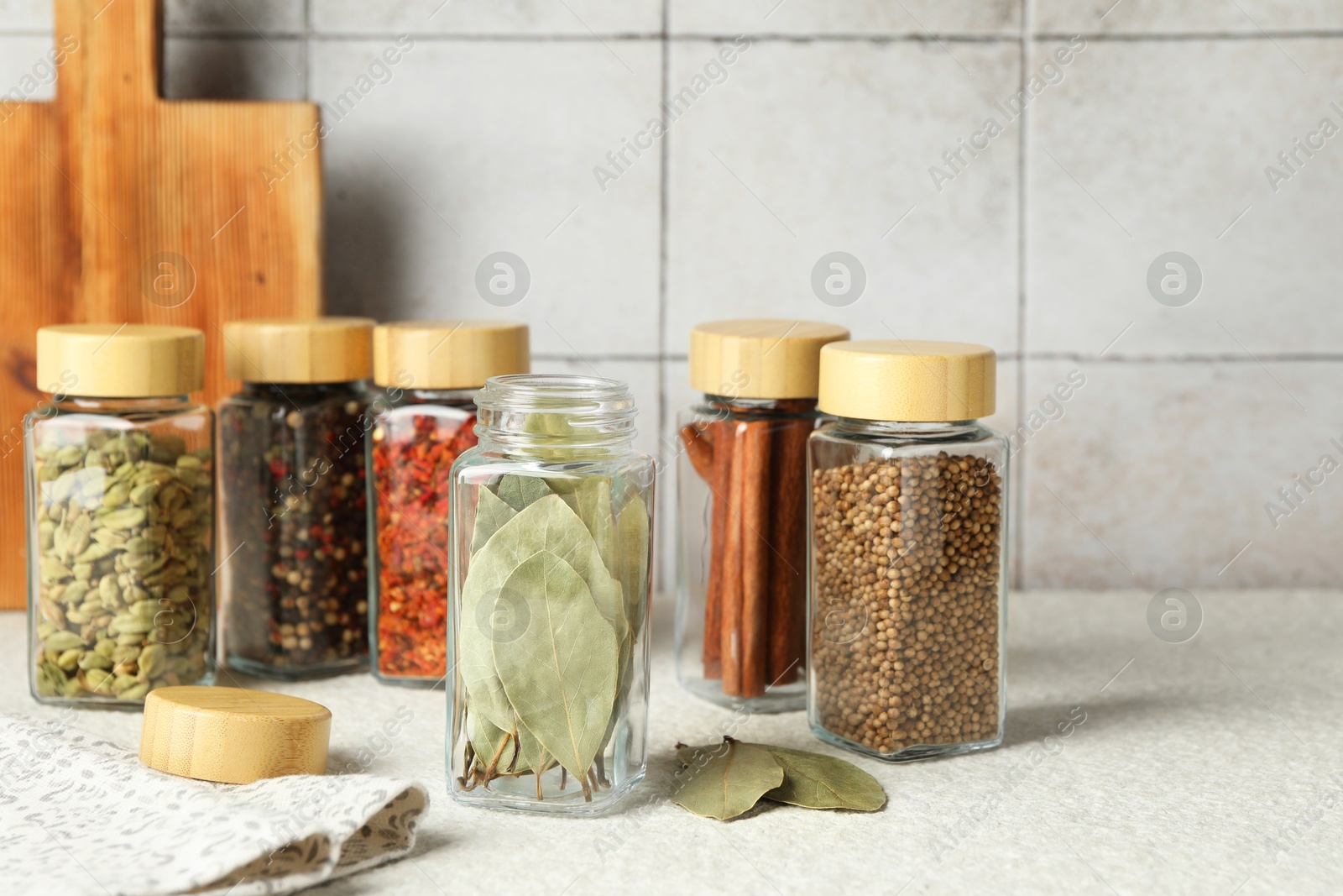 Photo of Different spices in glass jars on light textured table, closeup