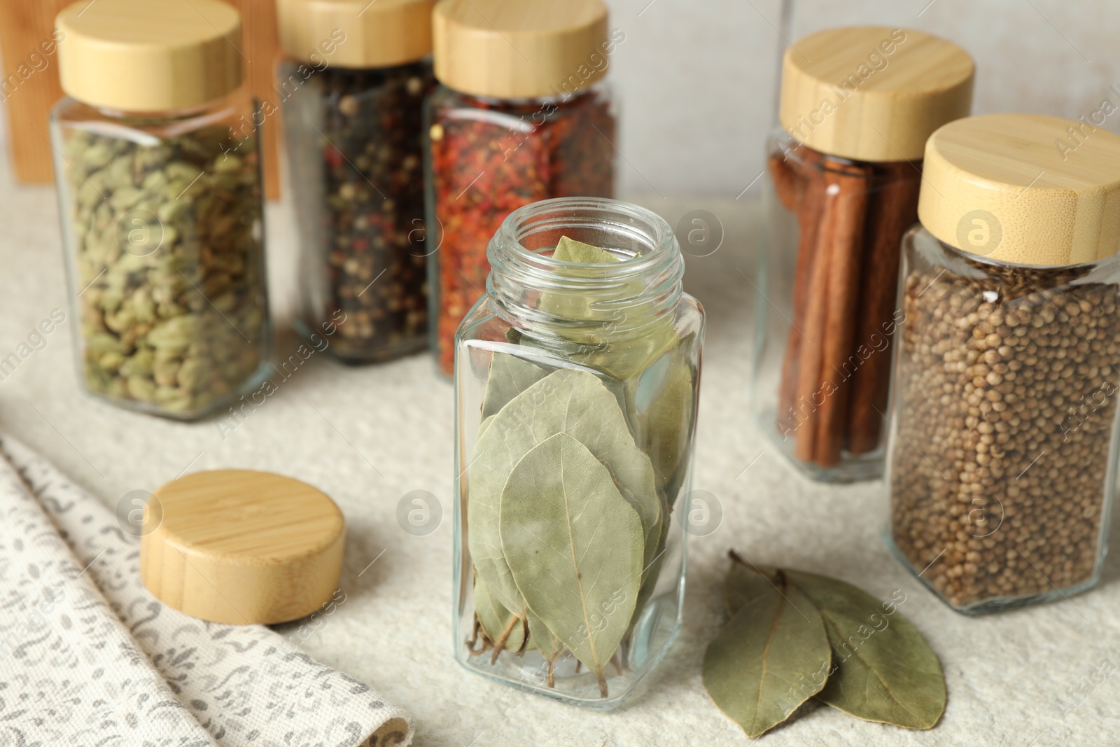 Photo of Different spices in glass jars on light textured table, closeup