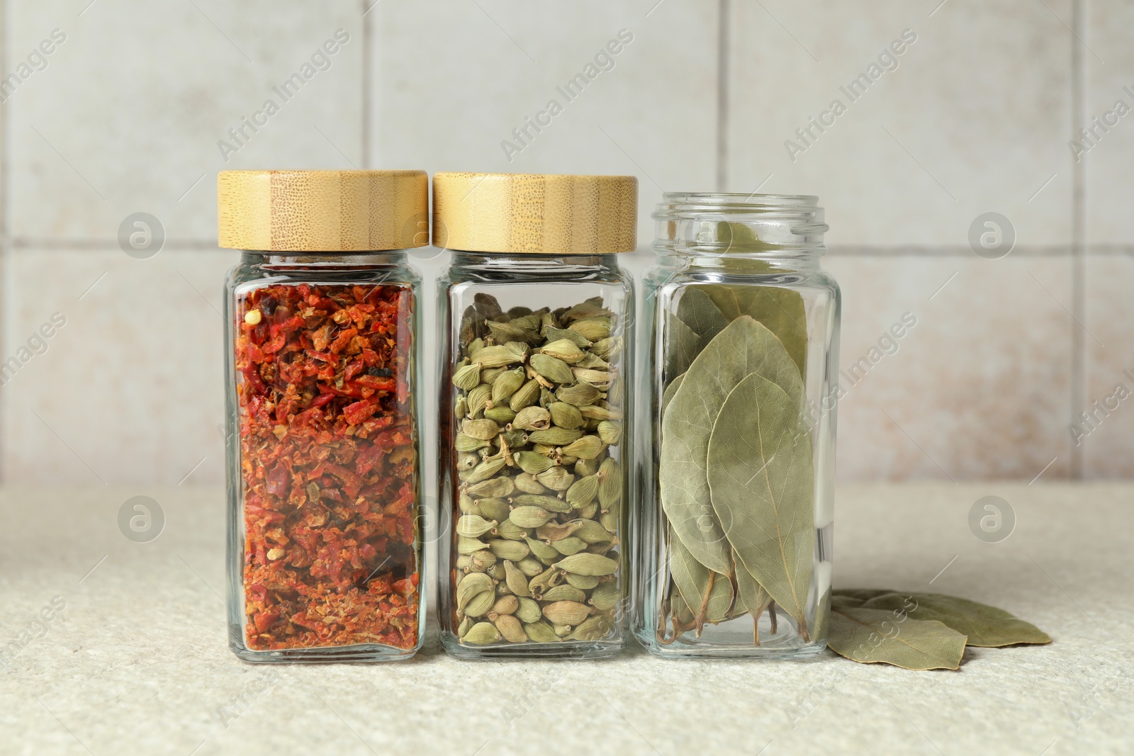 Photo of Different spices in glass jars on light textured table, closeup