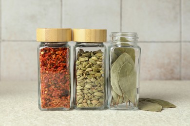 Different spices in glass jars on light textured table, closeup