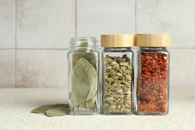 Different spices in glass jars on light textured table, closeup. Space for text