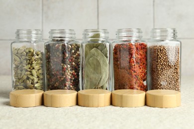 Different spices in glass jars and lids on light textured table, closeup