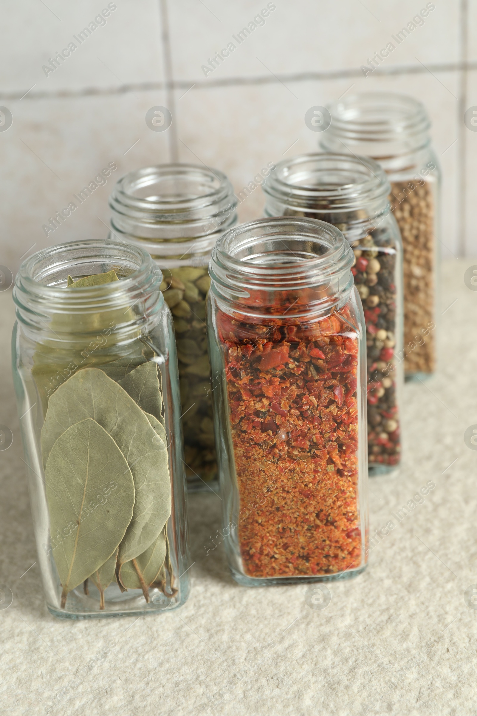 Photo of Different spices in glass jars on light textured table, closeup