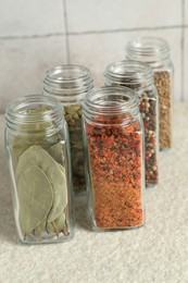 Different spices in glass jars on light textured table, closeup