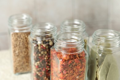 Different spices in glass jars on table, closeup