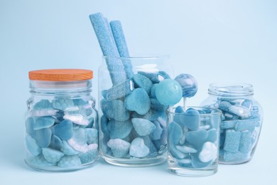 Many bright candies in glass jars on light blue background