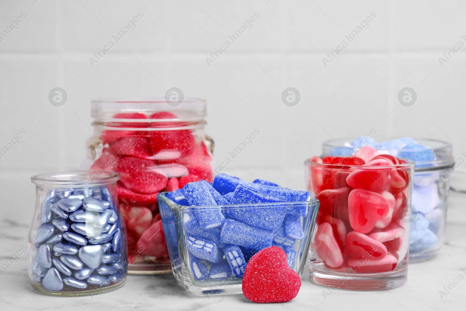 Image of Many bright candies in glass jars on white marble table