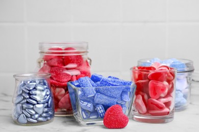 Many bright candies in glass jars on white marble table