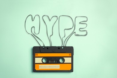 Illustration of Hype word made of audio cassette tape on light turquoise background, top view