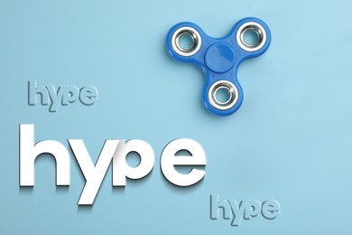 Hype words and spinner on light blue background, top view