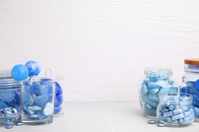 Many blue color candies in glass jars on light tiled table. Space for text