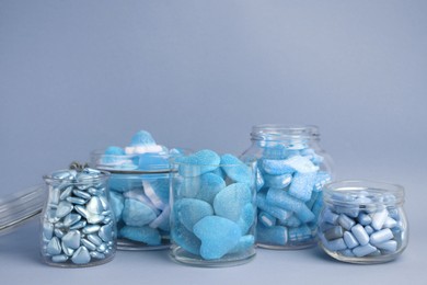 Image of Many bright candies in glass jars on light blue background. Space for text