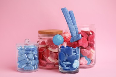 Image of Many bright candies in glass jars on pink background