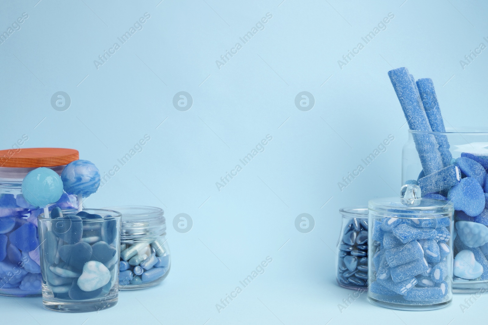 Image of Many bright candies in glass jars on light blue background. Space for text