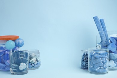 Many bright candies in glass jars on light blue background. Space for text