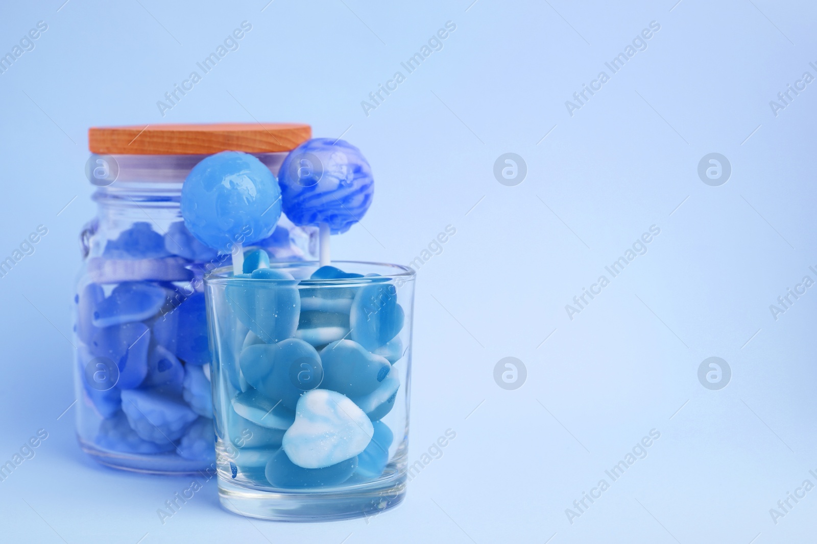 Image of Many bright candies in glass jars on light blue background. Space for text