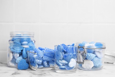 Many blue color candies in glass jars on white marble table. Space for text