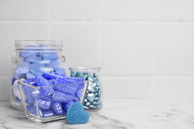 Many blue color candies in glass jars on white marble table. Space for text