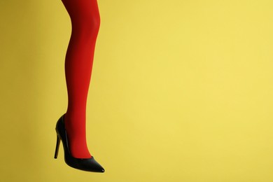 Photo of Woman wearing bright tights and high heel shoe on yellow background, closeup. Space for text