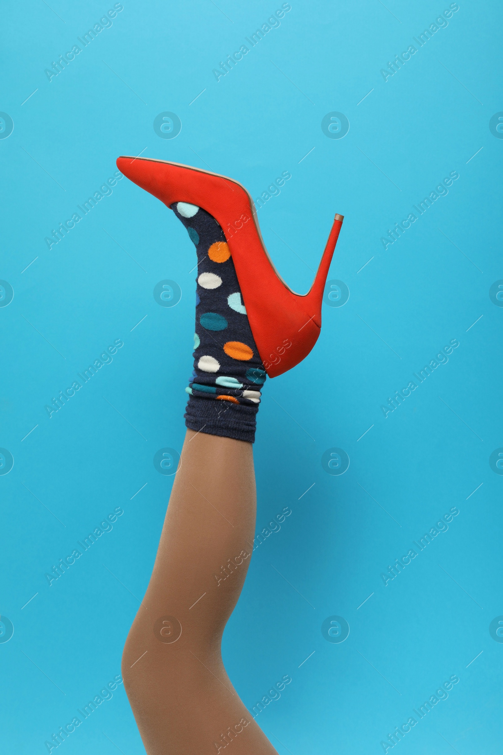 Photo of Woman wearing sock and high heel shoe on light blue background, closeup