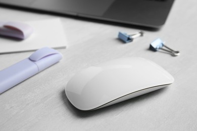 Photo of Wireless mouse and stationery on light wooden table, closeup