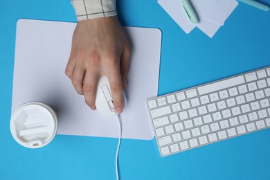 Photo of Man with mouse, takeaway cup, stationery and computer keyboard at light blue table, top view