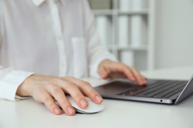 Woman working with wireless mouse and laptop at white table indoors, closeup