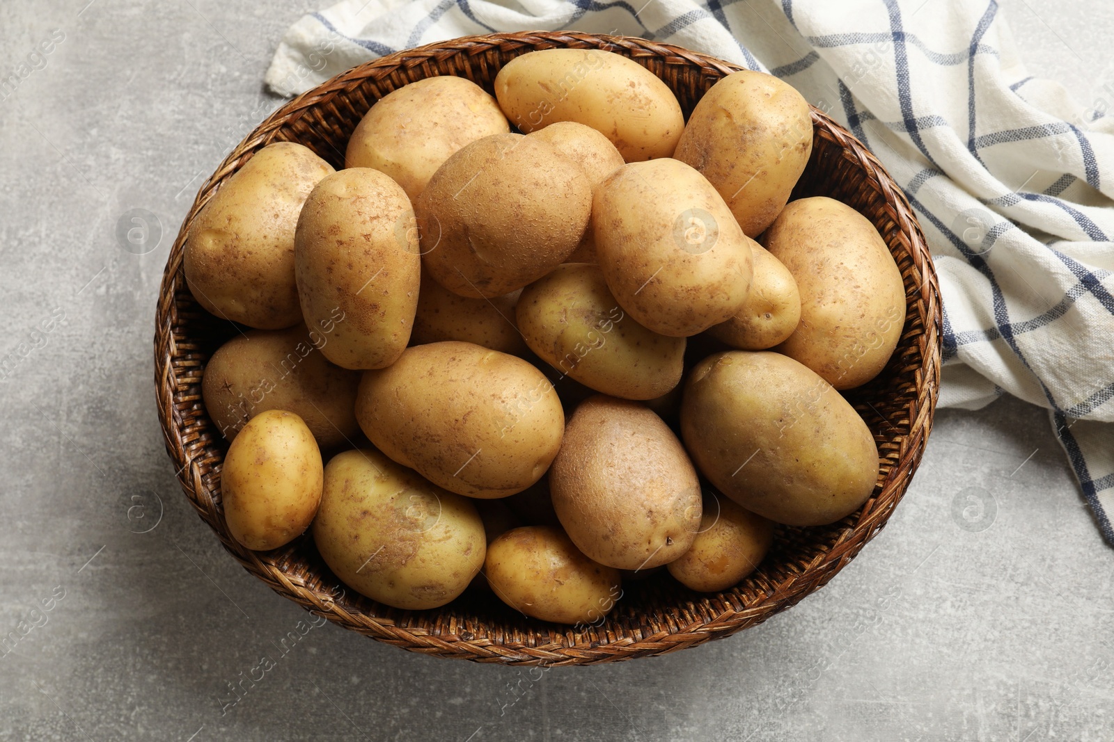 Photo of Many fresh potatoes in wicker basket on grey table, top view