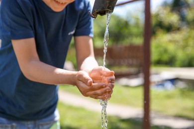 Photo of Water scarcity. Little boy drawing water with hands from tap outdoors, closeup. Space for text