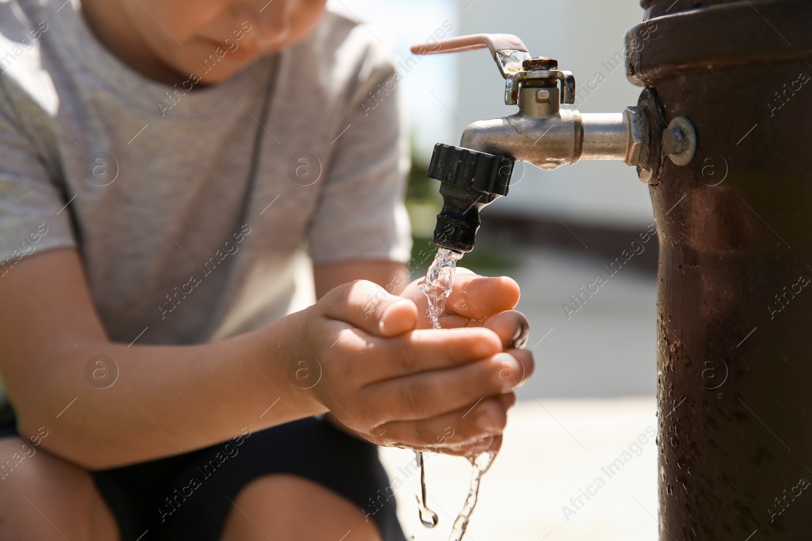 Photo of Water scarcity. Little boy drinking water from tap outdoors, closeup