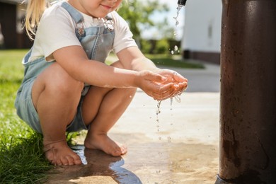 Photo of Water scarcity. Little girl drawing water with hands from tap outdoors, closeup