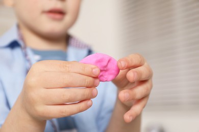 Photo of Little boy sculpting with play dough indoors, closeup