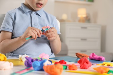 Photo of Little boy sculpting with play dough at table indoors, closeup