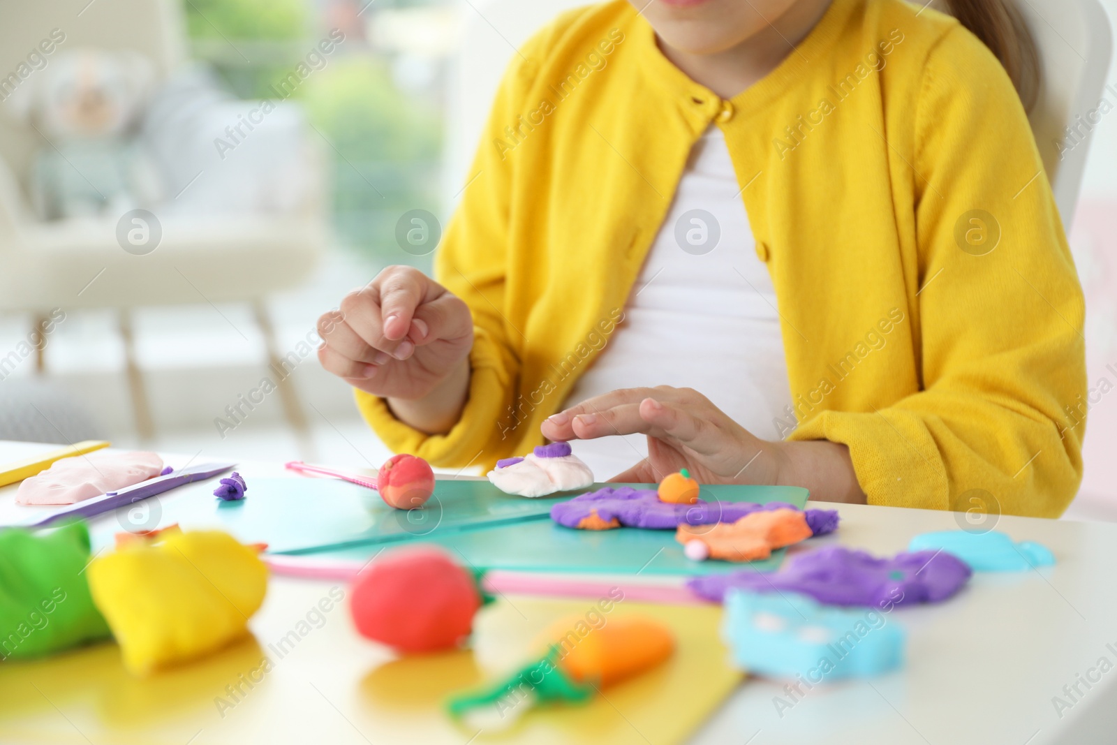 Photo of Little girl sculpting with play dough at table indoors, closeup