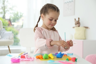 Little girl sculpting with play dough at table in kindergarten