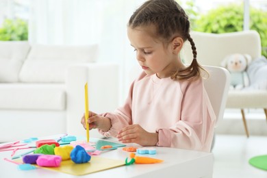 Little girl sculpting with play dough at table in kindergarten