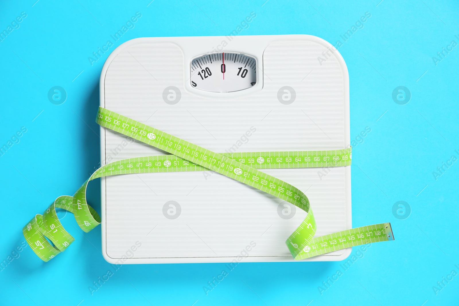 Photo of Scale tied with measuring tape on light blue background, top view